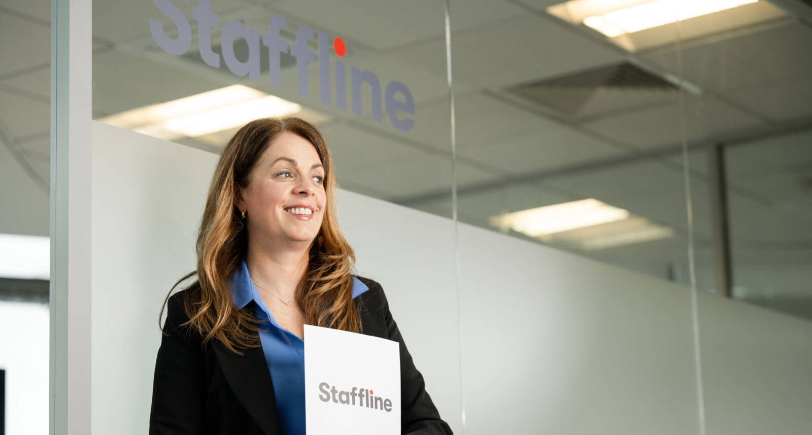 Team member smiling at Staffline office entrance and holding a Staffline booklet