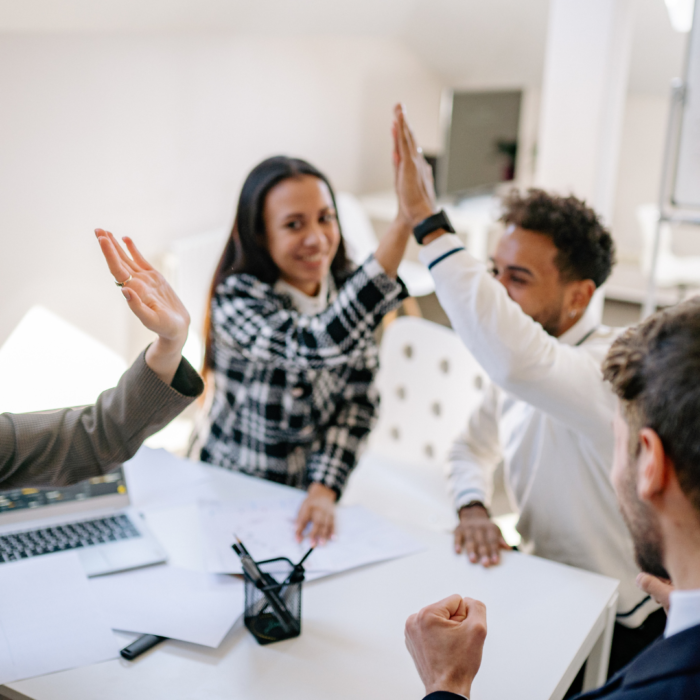 A group of diverse colleagues are celebrating a successful outcome, raising their hands in a high-five gesture.

The scene is composed around a white table, with several people seated around it.  The individuals' positions and actions suggest a collaborative meeting or team gathering.  The focus is centered on the collaborative high-five, with arms raised in the air.  The perspective is from slightly above the table, capturing a dynamic interaction among the group.  The framing emphasizes the moment of celebration, positioning the participants in a close-knit arrangement. Elements are positioned around the high-five action, emphasizing the dynamic nature of the moment.

The key subjects are multiple people of various ethnicities.  They are dressed in casual business attire, displaying expressions of joy and excitement.  The individuals appear to be engaged in a shared moment of triumph, high-fiving and expressing pride and cooperation. 


The artistic medium is photography, likely taken with a smartphone or a camera. The technical execution is sharp and well-lit, capturing the details of the scene.  The style is candid and naturalistic, focused on the group interaction.  No creative choices that go beyond the natural capture of the celebration are evident.

The setting is an office or a similar indoor workspace. The lighting is bright and even, casting no significant shadows, suggesting an office space with overhead lights.  The atmosphere is one of success and accomplishment, with the collaborative action creating a joyful and positive mood.