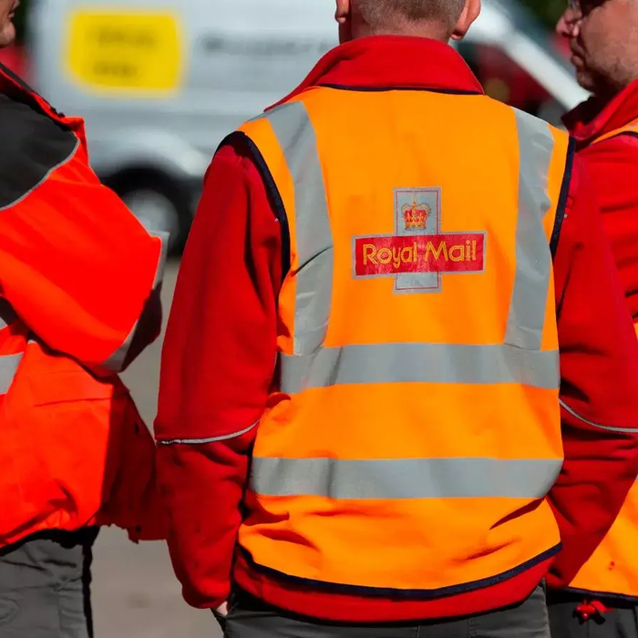 Three Royal Mail postal workers wearing orange and red high-visibility jackets stand together outdoors, preparing for their delivery shift.