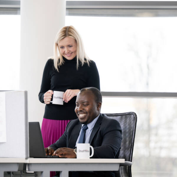 Two Staffline team members smiling together while working on computer