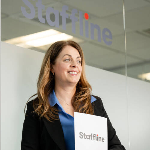 Team member smiling at Staffline office entrance and holding a Staffline booklet