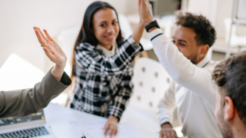 A group of diverse colleagues are celebrating a successful outcome, raising their hands in a high-five gesture.

The scene is composed around a white table, with several people seated around it.  The individuals' positions and actions suggest a collaborative meeting or team gathering.  The focus is centered on the collaborative high-five, with arms raised in the air.  The perspective is from slightly above the table, capturing a dynamic interaction among the group.  The framing emphasizes the moment of celebration, positioning the participants in a close-knit arrangement. Elements are positioned around the high-five action, emphasizing the dynamic nature of the moment.

The key subjects are multiple people of various ethnicities.  They are dressed in casual business attire, displaying expressions of joy and excitement.  The individuals appear to be engaged in a shared moment of triumph, high-fiving and expressing pride and cooperation. 


The artistic medium is photography, likely taken with a smartphone or a camera. The technical execution is sharp and well-lit, capturing the details of the scene.  The style is candid and naturalistic, focused on the group interaction.  No creative choices that go beyond the natural capture of the celebration are evident.

The setting is an office or a similar indoor workspace. The lighting is bright and even, casting no significant shadows, suggesting an office space with overhead lights.  The atmosphere is one of success and accomplishment, with the collaborative action creating a joyful and positive mood.