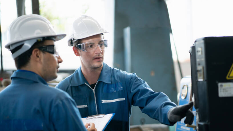 Two engineers wearing helmets and protective eyewear at work