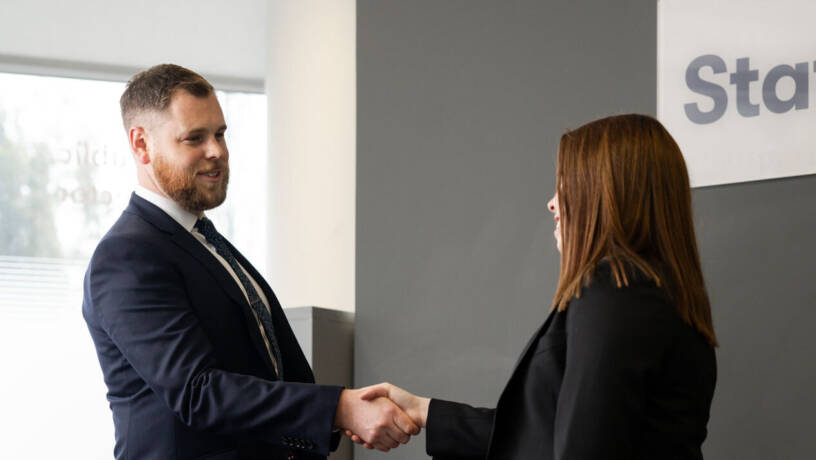 Two people greeting each other with a handshake in front of a Staffline wall sign